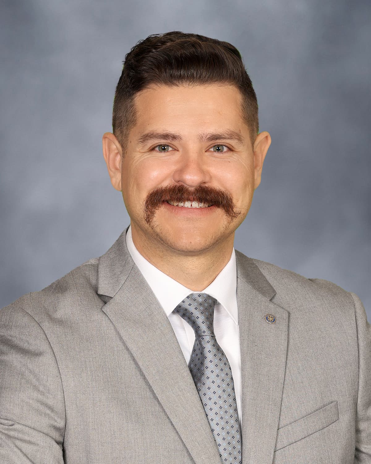 Studio portrait of auctioneer Beto Beas wearing a tan suit and tie