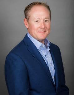 Studio portrait of auctioneer Gil Hyder wearing a navy suit and light blue shirt