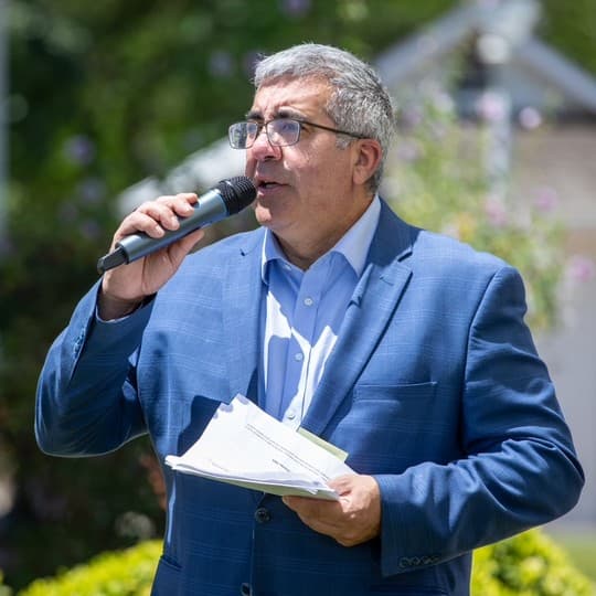 Broadcaster and charity benefit host Sal Castaneda speaking into a handheld microphone at an outdoor event