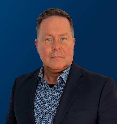 Studio portrait of auctioneer Tony Shaw in a dark blazer against a blue background