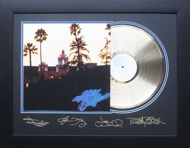 Framed gold record displayed beside the The Eagles Hotel California album cover with a laser-reproduced signature, offered as a charity auction lot