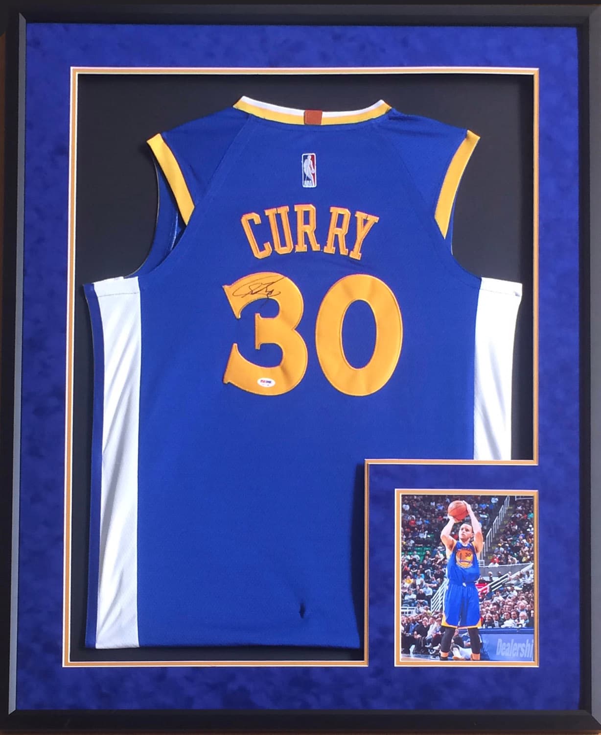 Blue and gold Golden State Warriors jersey hand-signed by Stephen Curry, framed with action photographs, offered as a charity auction lot